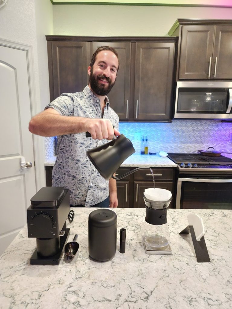 Bryan Kofsky joyfully pouring water for coffee using a new matte black coffee setup on kitchen island on June 9, 2023.